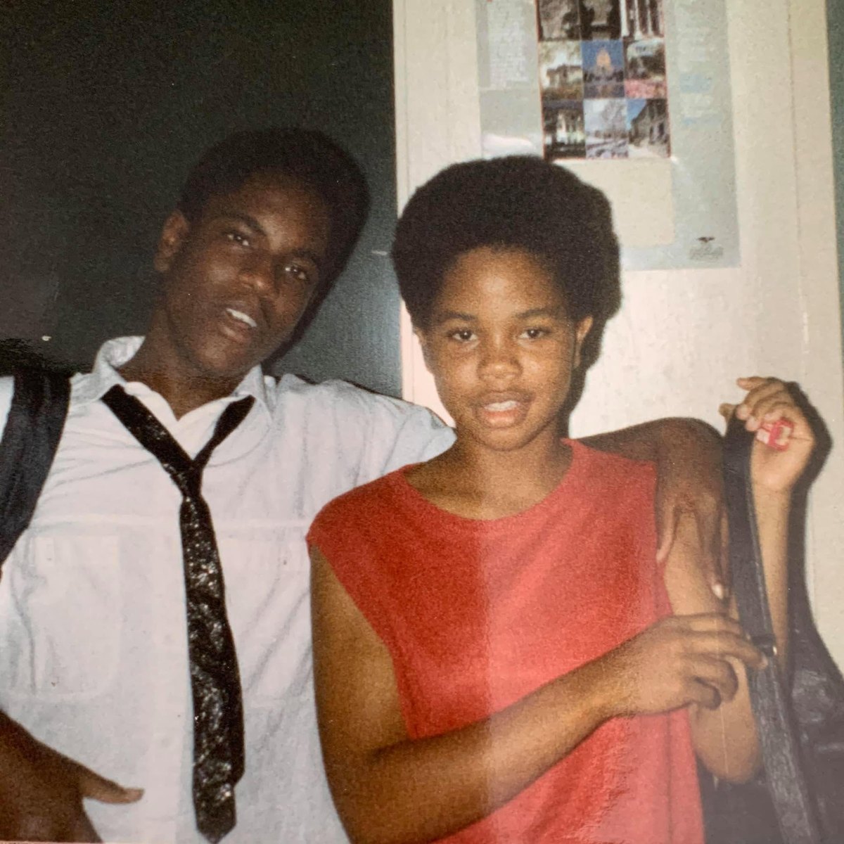 Two students posing side by side indoors, one in a white shirt and patterned tie, the other in a red sleeveless top