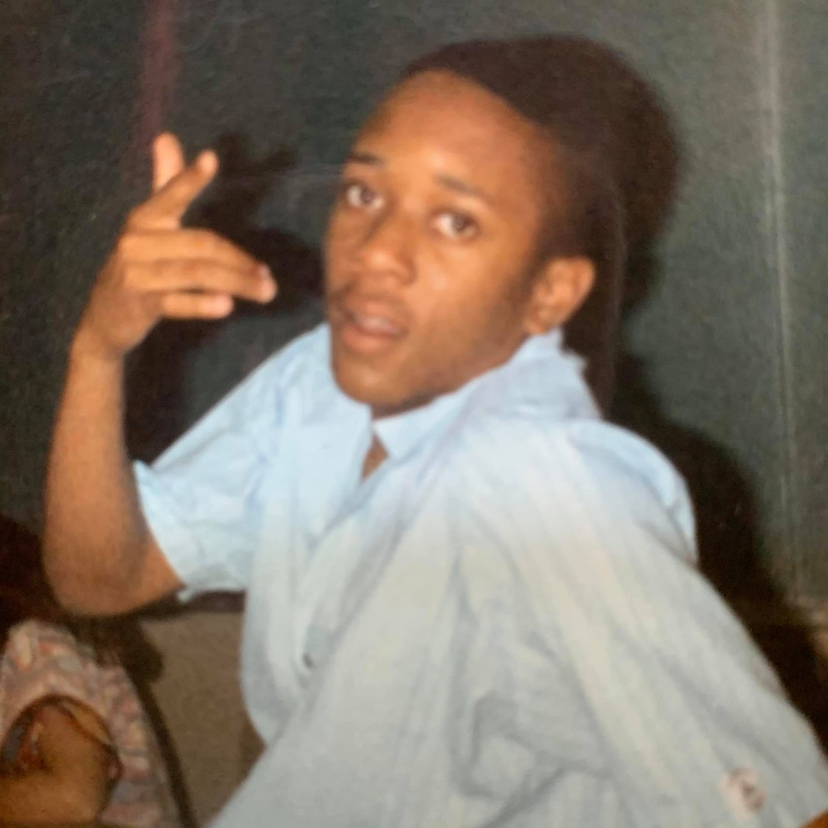 A student in a light-blue button-down shirt gesturing toward the camera
