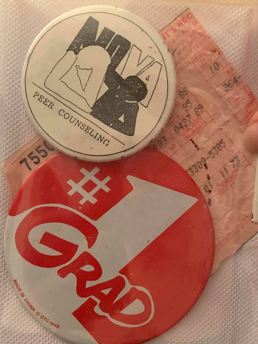 Two vintage pin-back buttons — a Nova peer counseling pin and a red '#1 Grad' pin — resting on a paper sleeve